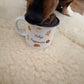 Dog sniffing a mug labelled 'Holly's Puppuccino' on a soft surface