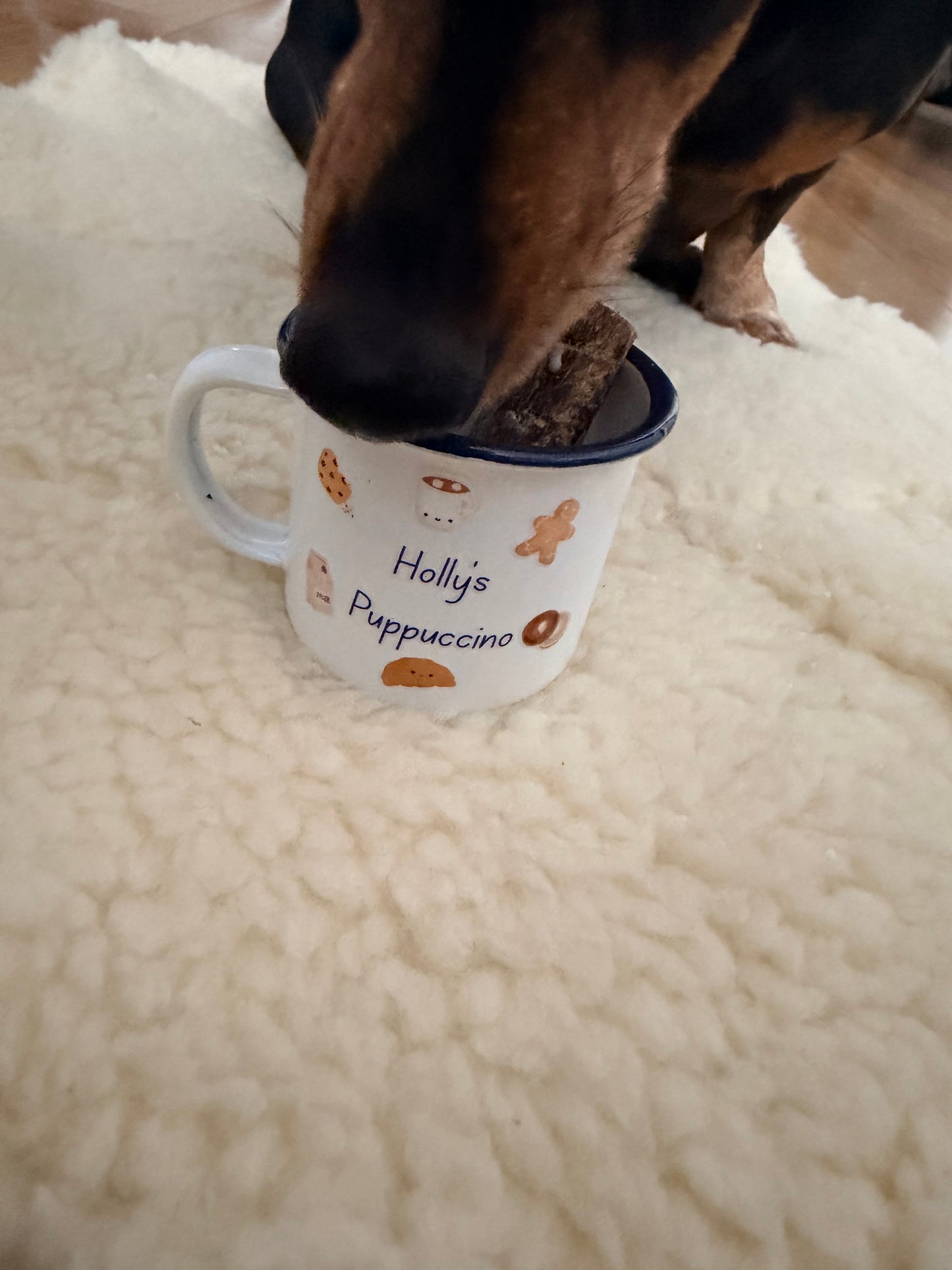 Dog sniffing a mug labelled 'Holly's Puppuccino' on a soft surface
