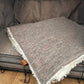 Gray textured throw blanket with white fringe draped over a gray sofa.