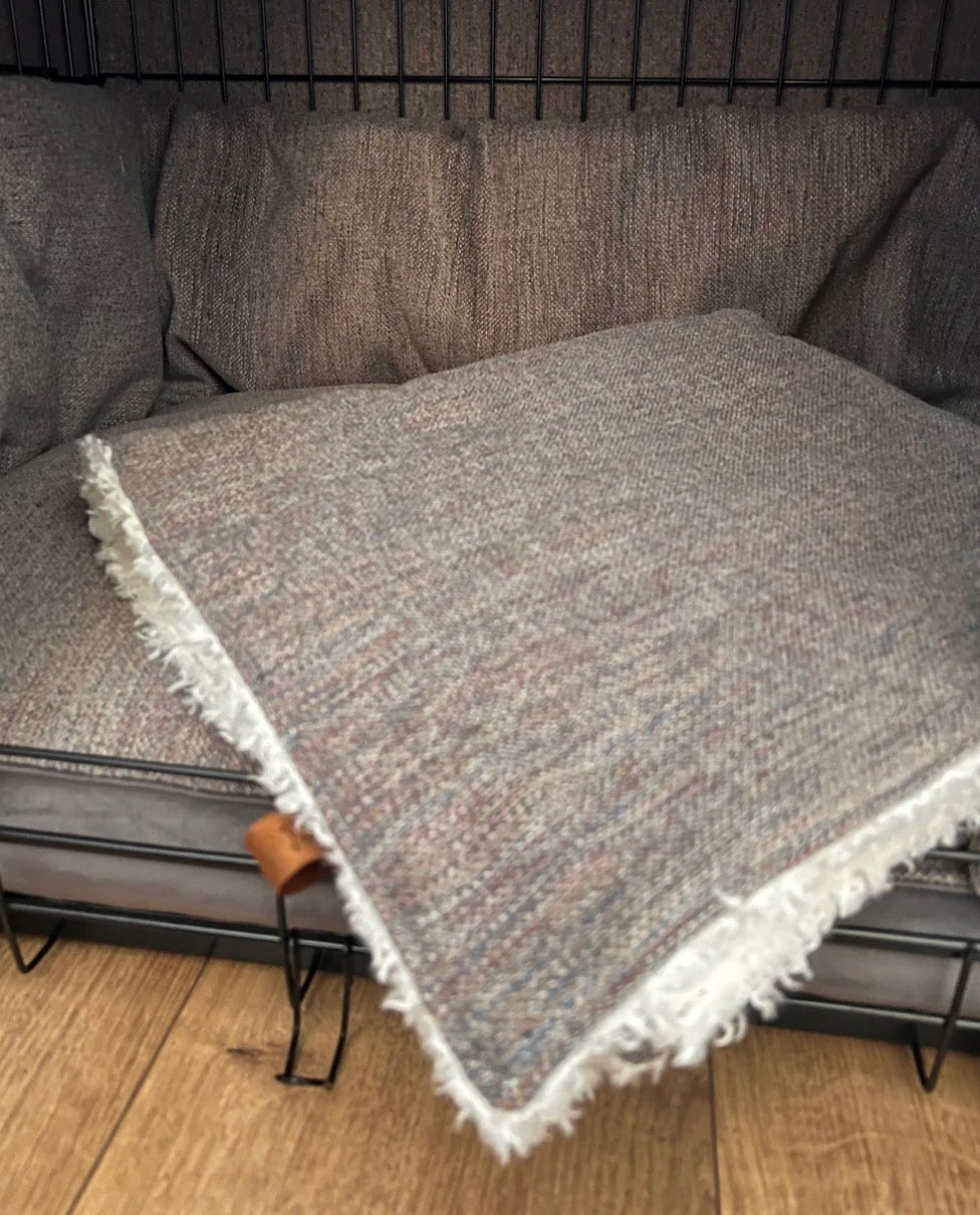 Gray textured throw blanket with white fringe draped over a gray sofa.