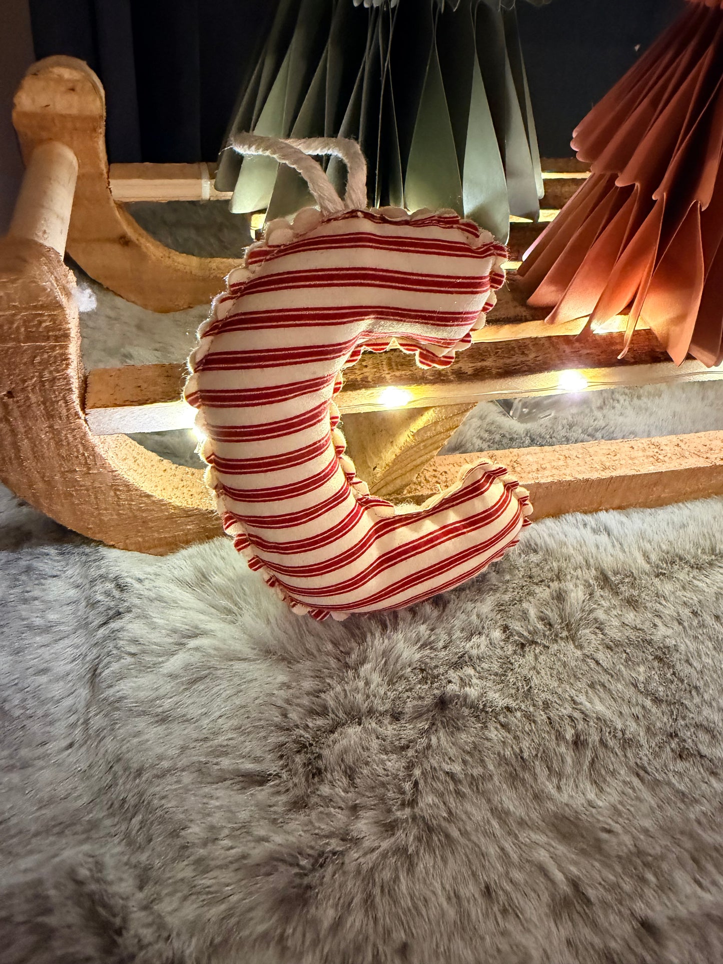 Decorative wreath with red and white stripes hanging on a wooden frame against a textured wall.